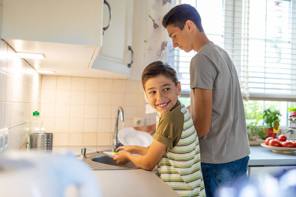 Dos chicos lavando los platos en el fregadero de la cocina
 - Foto, Imagen