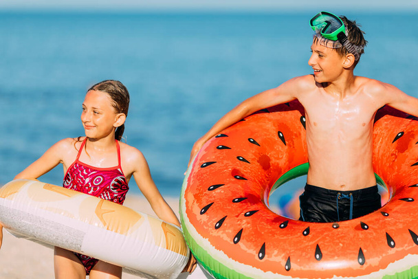 Happy kids brother and sister have fun on the beach with inflatable swimming circles. summer holidays - Fotó, kép