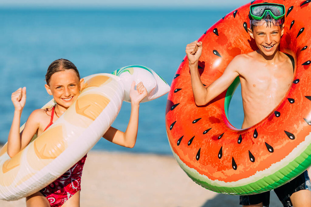 Happy children a little boy and girl have fun on the beach with inflatable swimming circles, show a winning gesture. Travel, summer holidays - Photo, image