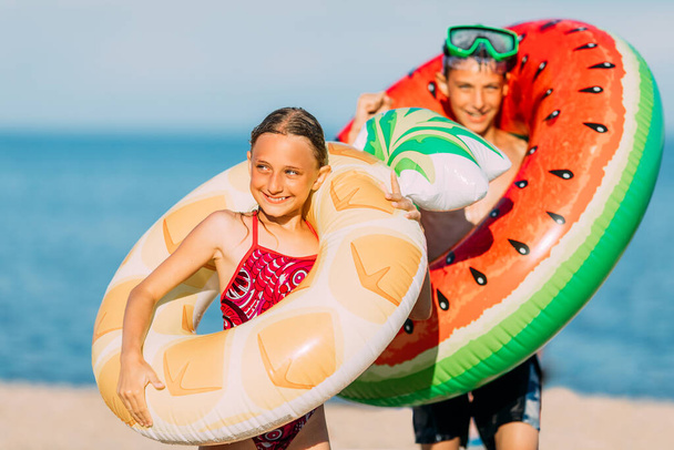 Happy kids little boy and girl have fun on the beach with inflatable swimming circles. summer holidays - Fotografie, Obrázek