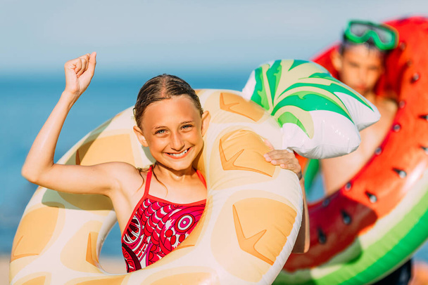 Happy children a little boy and girl have fun on the beach with inflatable swimming circles, show a winning gesture. Travel, summer holidays - 写真・画像
