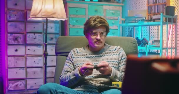 Blanke man nerd in bril en met snor zittend voor vintage TV monitor en videogame spelend met joystick. Mannelijke domme gek verliezen in het spel. Retro stijl van de jaren 80. Gamer loser uit de jaren 90 - Video