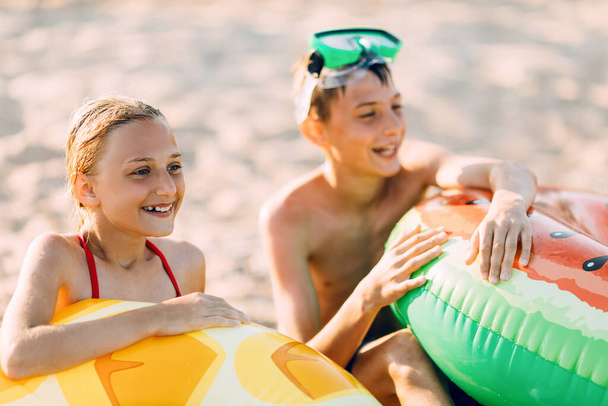 kids brother and sister with an inflatable circle, play and have fun sitting on the sand on the beach - Fotoğraf, Görsel