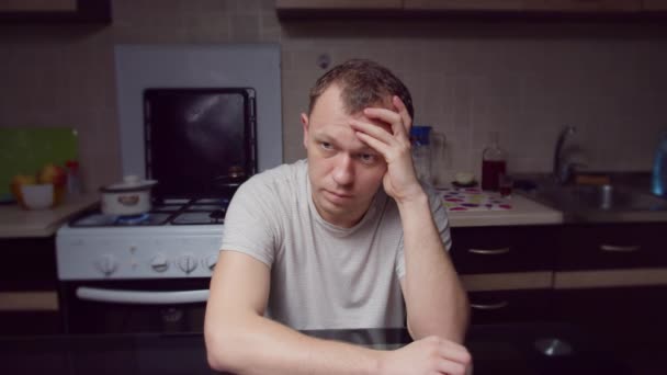 Trieste man zit in de avond aan de keuken aan de tafel, ondergedompeld in zijn problemen - Video