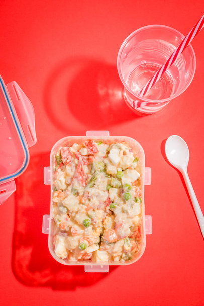 Plastic container with Russian salad and plastic utensils with red background. - Photo, Image