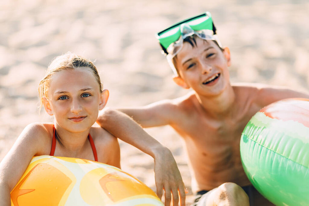 Happy children boy and girl in swimming glasses with inflatable circle, play and have fun sitting on the sand on the beach enjoy summer vacation - Foto, afbeelding