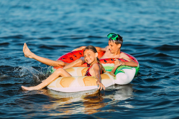 Yüzme, yaz tatili mutlu çocuklar ve kızlar şişirilebilir dairelerle denizde oynayıp yüzüyorlar. Yaz tatili - Fotoğraf, Görsel