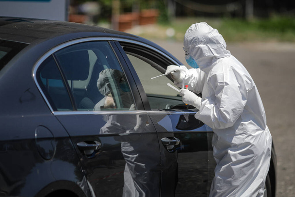 Bucharest / Romania - July 11, 2020: A health worker uses a CPR test (mouth and nasal swab) on a person inside a car to determine the presence or absence of the Covid-19. - Foto, Bild