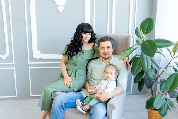 Genç ebeveynler bebeklerini yeşil elbiseli parlak bir odada kucaklıyor. Mutlu aile kavramı, aile günü.. - Fotoğraf, Görsel