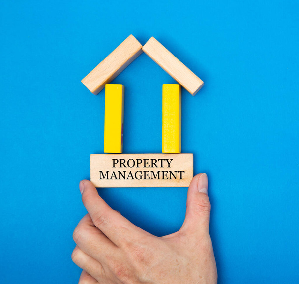 Main masculine plaçant une gestion immobilière dans une maison faite de blocs de bois dans une image conceptuelle du marché immobilier. Sur fond bleu. - Photo, image