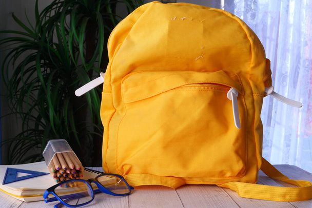 πίσω στο σχολείο έννοια με κίτρινο σακίδιο πλάτης και τους προμηθευτές του σχολείου στο τραπέζι  - Φωτογραφία, εικόνα