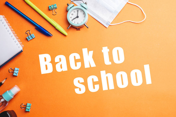 Briefpapier-Schulbedarf rund um die Worte "Zurück zur Schule" auf orangefarbenem Hintergrund. Ansicht von oben. - Foto, Bild