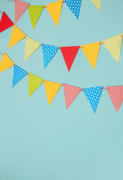 Festive garland of multi-colored paper flags on a blue background. Birthday greeting card with copy space. - Foto, imagen