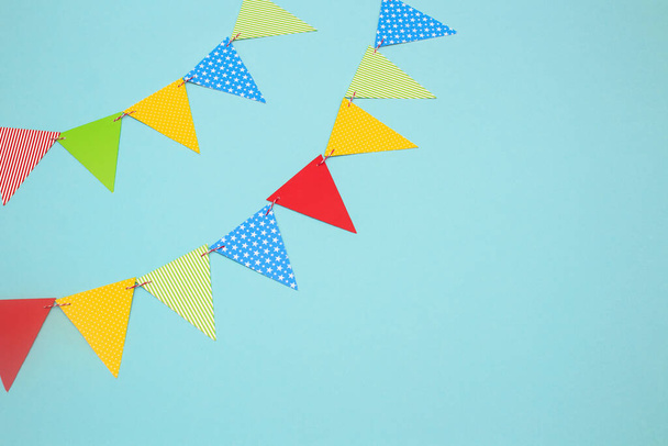 Festive garland of multi-colored paper flags on a blue background. Birthday greeting card with copy space. - Foto, imagen