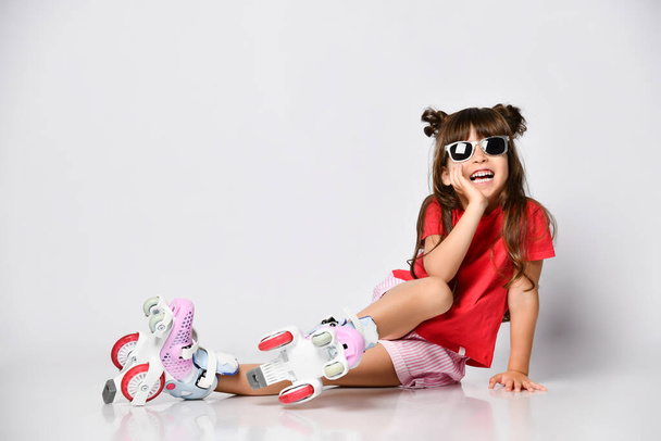 Beautiful girl posing sitting on the floor, in a red t-shirt and shorts and a fashionable hairstyle, in roller skates on her feet - Fotoğraf, Görsel