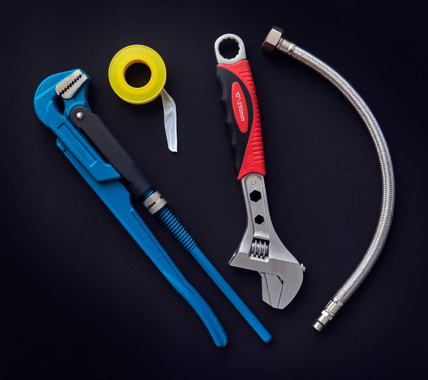 Tools, adjustable wrenches, flexible hose and  thread seal tape on dark background, toned - Photo, Image