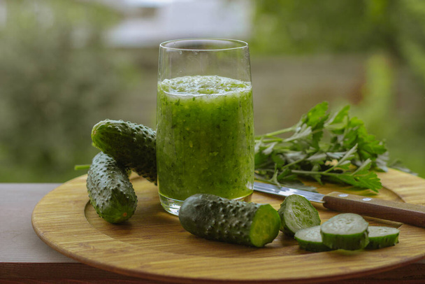 Leckere gesunde grüne Gemüsesaft mit Gurken aus frischen Zutaten gemischt und serviert in einem hohen Glas auf einem Tisch im Freien in einem Sommergarten - Foto, Bild