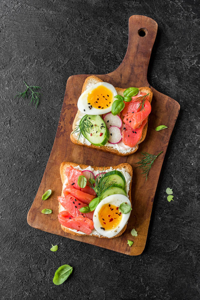Healthy open salmon sandwich with cream cheese, soft egg, veggies and greens. Delicious protein fish sandwich for breakfast or brunch, top view, copy space. - Fotografie, Obrázek