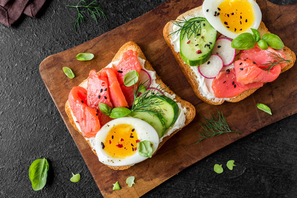 Healthy open salmon sandwich with cream cheese, soft egg, veggies and greens. Delicious protein fish sandwich for breakfast or brunch, top view, copy space. - Фото, зображення
