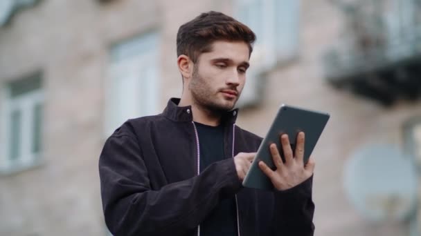 Smiling guy reading message tablet outdoors. Happy man using tablet on street - Footage, Video
