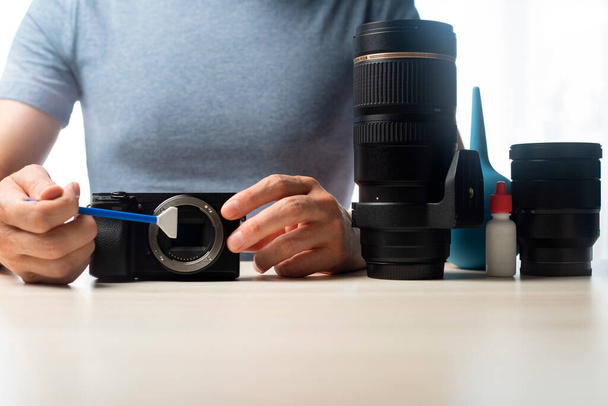 Person cleaning mirrorless digital camera with swab and lens. Technology concept - Zdjęcie, obraz