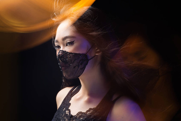 Beautiful Asian girl portrait in a black face protective mask. Trendy fashion accessory. Protective design. Vogue photoshoot. coronavirus protection covid 19 pandemic quarantine - Foto, afbeelding