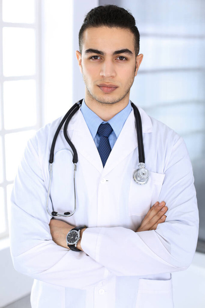 Arab doctor man standing with crossed arms in medical office or clinic. Medicine and healthcare concept - Fotó, kép