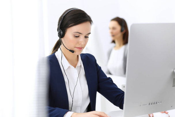 Call center. Beautiful woman receptionist sitting in headset at customer service office. Group of operators at work. Business concept - Fotografie, Obrázek