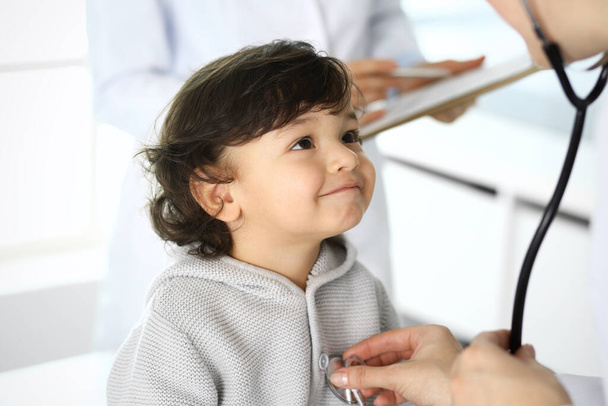 Doctor examining a child patient by stethoscope. Cute arab boy at physician appointment. Medicine and healthcare concept - Foto, Imagem