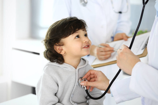 Doctor examining a child patient by stethoscope. Cute arab boy at physician appointment. Medicine and healthcare concept - Zdjęcie, obraz