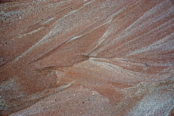 Primer plano de los patrones ondulados de agua y arenas marrones y blancas rojizas en una playa
. - Foto, Imagen