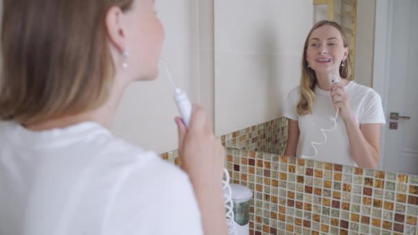 Χαμογελαστή νεαρή γυναίκα με σιδεράκια που καθαρίζει τα δόντια της με αρδευτικό νερού - Πλάνα, βίντεο