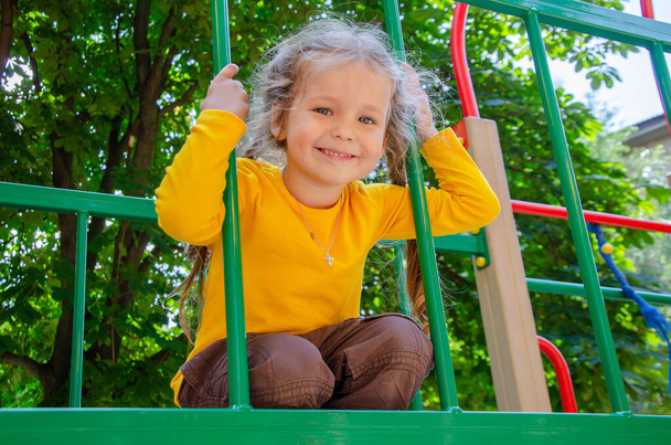 Schöne Mädchen im gelben T-Shirt spielt auf dem Spielplatz, das Kind ruht sich an der frischen Luft aus. - Foto, Bild