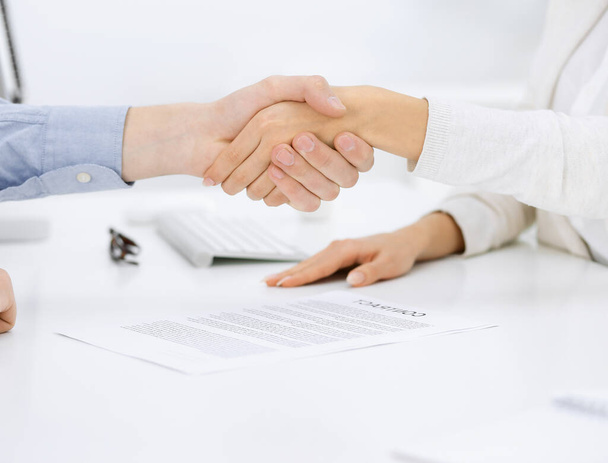 Casual dressed businessman and woman shaking hands after contract signing in white colored office. Handshake concept - Foto, imagen