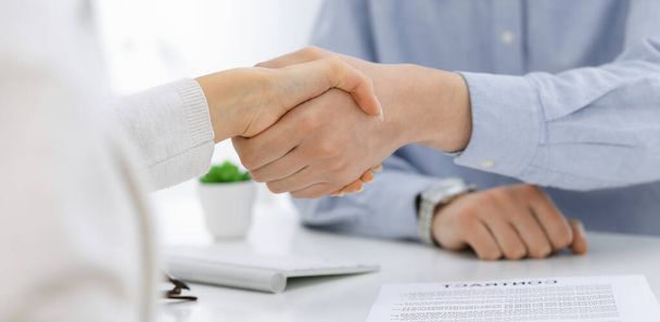 Casual dressed businessman and woman shaking hands after contract signing in white colored office. Handshake concept - Φωτογραφία, εικόνα
