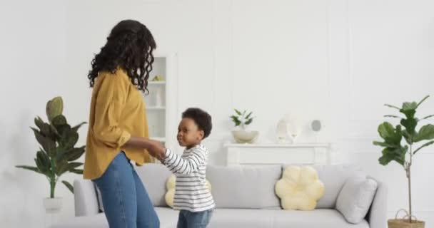 幸せな陽気なアフリカ系アメリカ人の母親は、ロックダウン中に自宅のリビングルームで娘と踊って楽しんでいます。小さなかわいい子供と一緒にママダンスや笑い。音楽を楽しむ小さな喜びの子供. - 映像、動画
