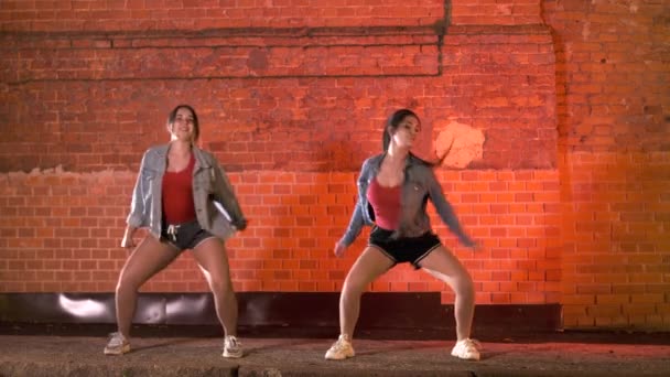 Две красивые веселые женщины танцуют современную хореографию, вечером уличные танцы у кирпичной стены. Молодежная субкультура
 - Кадры, видео