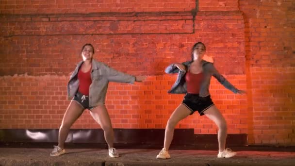 duas belas mulheres alegres dançando coreografia moderna, dança de rua contra uma parede de tijolo à noite. Subcultura da juventude
 - Filmagem, Vídeo