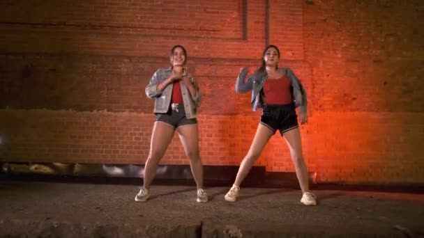 Две счастливые девушки танцуют современную хореографию, уличные танцы против кирпичной стены ночью. Молодежная субкультура. Гимбальный выстрел
 - Кадры, видео