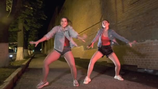 Két fiatal lány utcai táncot jár egy városi parkban esténként. Ifjúsági szubkultúra. Kortárs koreográfia. Gimbal lövés. - Felvétel, videó