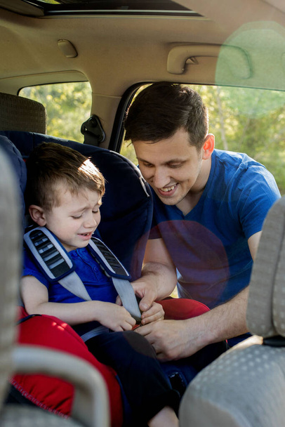 Close-up shot of concentrated father helping his son to fasten belt on car seat. Child transportation safety. - Foto, Imagem