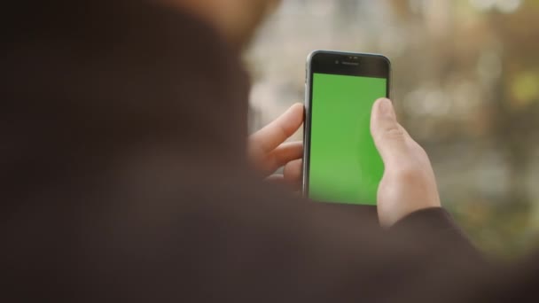 Muž projíždí zelenou obrazovku chytrého telefonu. Guy surfování na internetu maká na mobilu - Záběry, video