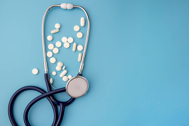Stethoscope and many pills on blue background with copy space. - Photo, image