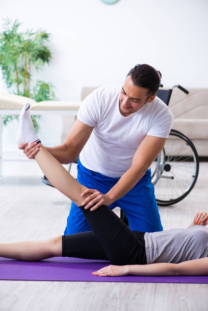 Мужской физиотерапевт делает упражнения с травмированной женщиной на полу - Фото, изображение