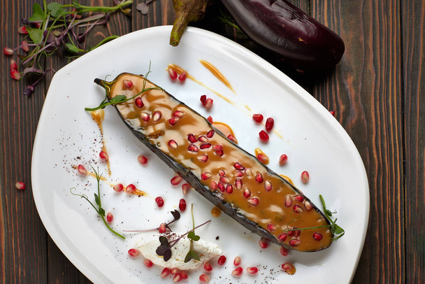Baked eggplant with cheese and pomegranate seeds, on a white plate, on wooden background - Foto, Bild