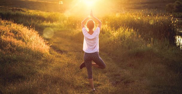 mulher em uma pose de ioga ao pôr do sol pela atenção plena à beira do lago e saúde mental
 - Foto, Imagem