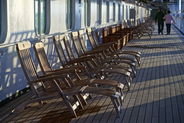Um casal idoso passeia por uma longa fila de cadeiras vazias no convés do passeio de um navio de cruzeiro
. - Foto, Imagem
