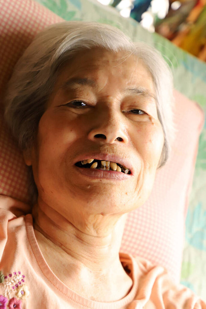glimlachende senior vrouw kijken naar camera ontspannen in verpleegkundig bed - Foto, afbeelding