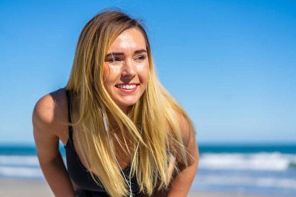 A gorgeous bikini model posing in a beach environment wearing headphones, listening to her favorite music - Fotó, kép