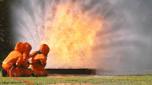 Firefighter fighting with flame using fire hose chemical water foam spray engine. Fireman wear hard hat, body safe suit uniform for protection. Rescue training in fire fighting extinguisher - Photo, Image